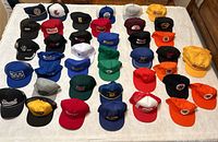 Overview of the 40 vintage trucker hats arranged in five rows on white background, showing various corporate and industry logos in different colors and styles.