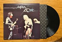 Front cover of Golden Earring Mad Love vinyl album with record partially pulled out showing black inner sleeve with repeated white logo pattern.