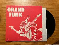 Front of the red album cover showing band members and "GRAND FUNK" lettering with vinyl partially visible.