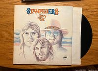 Front cover of The Stampeders New Day vinyl album showing illustrated portraits of the band members, record partially visible.