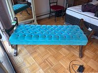 Front view of the teal tufted velveteen seat on the wooden bench through a window-lit room.