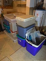 Photo showing stacked plastic storage bins with various colors and lids, including the large wheeled clear bin at the bottom.