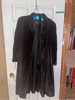 Full view of the dark brown mink fur coat hung on hanger on a door.