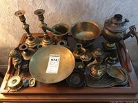 Top view of tray with two brass candlesticks, two brass bowls including hammered bowl, Turkish samovar with wooden handle, brass mortar and pestle, cherub figurine, barometer, and other small brass items
