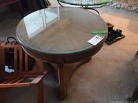 Full view of the round wood coffee table with clear glass top showing the wooden legs and frame.