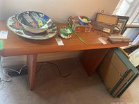 Full front view of teak console table with decorative ceramic bowls, green ceramic planter, vintage wooden items, and books on top.
