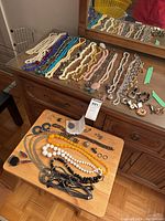 Wide view of dresser surface and small table showing necklaces, earrings, brooches, bracelet, pin