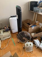 Photo of Garrison dehumidifier, Honeywell tower fan, PowerMax desk fan and small space heater placed on wooden floor near cardboard boxes.