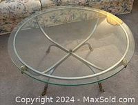 Front view of the round glass coffee table showing the clear glass top and the silver-colored metal base with brass detailing on feet and supports.