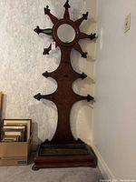 Full front view of wooden hall stand showing circular mirror, multiple coat hooks, and umbrella tray at base