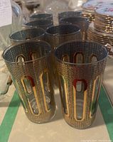 Eight Culver Tiffany signed highball glasses with 22k gold detailing arranged in a group, showcasing the blue hue and ornate gold pattern.