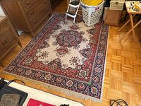 Area rug with traditional medallion and floral pattern placed on wooden floor, showing worn condition and fringe edges, with surrounding furniture visible.