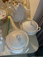 Two white ceramic tureens with lids and an Adams tureen with lid and serving spoon on a table.