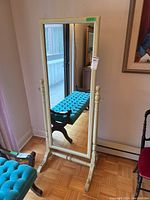 Front view of the standing mirror showing the painted wood frame and reflective surface. Mirror has decorative finials and curved base feet.