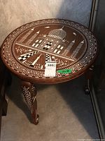 Side view showing full round tabletop with architectural inlaid design and carved decorated legs.