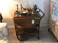 Front angle view of the wood tea cart holding various brass and metal items on the tray, showing wheels, handle and frame.
