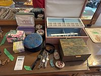 Lot on wooden table featuring five watches with different bands alongside multiple decorative jewelry and trinket boxes of varied sizes and colors, including a large pink patterned box and blue round box.