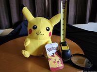 Front view of Pikachu plush with measuring tape showing approximately 10 inches height, original tag in front.