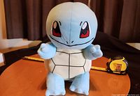 Front view of the 12-inch Squirtle soft plush toy on a wooden table showing facial details and front body.