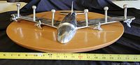 Front view of airplane-shaped metal coat hanger on wooden plaque with measuring tape showing about 22 inches width.