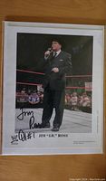 Full color photo of Jim Ross in a ring with red ropes, holding a microphone, signed by Jim Ross.