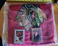 Folded red Adidas Chicago Blackhawks jersey in protective bag with two Connor Bedard trading cards
