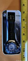 Front view of Edmonton Oilers watch in original NHL branded tin packaging, placed next to a tape measure showing approx. 9 cm length