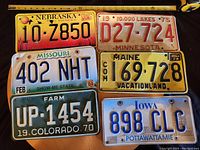 Photo showing six vintage U.S. license plates arranged on a surface with ruler for scale.