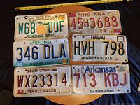 Photo showing six vintage U.S. license plates from different states with visible wear and varying years.