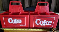Front view of two red plastic Coca-Cola bottle carriers showing Coca-Cola logos, each holding six 750ml bottles.