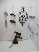 Full view of lot showing cast iron bell with cow figure, three-bell cast iron wind chime, heart-shaped cow bell wind chime, and additional hanging wind chimes and decorations