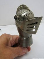 Side view of vintage medieval knight helmet bottle stopper with visor down, detailed metalwork visible, held in hand for scale.