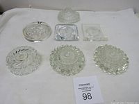 Seven vintage clear glass lamp bases shown on white cloth background.