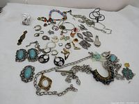 Wide view of various vintage and new broken jewelry pieces spread on white background showing earrings, necklaces, rings, bracelets, and charm parts.