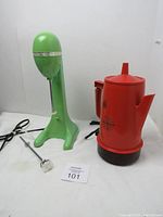 Photo showing the green Hamilton Beach milkshake mixer with its mixing rod detached placed on the table next to the orange Regal Poly Perk coffee percolator with starburst pattern.