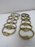 Front angle of 10 vintage women's bracelet style wristwatches laid flat showing faces and stretch metal bands in gold and silver tones.