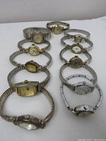 Eleven vintage women's bracelet style wristwatches arranged in two rows on white surface. Watches include gold-toned and silver-toned metal stretch bands, varying face shapes, and styles.