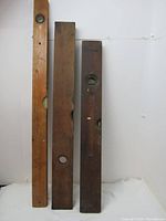 Three vintage wood and brass levels placed vertically against a white backdrop showing their front sides with visible circular bubble vials and aged wood surfaces.