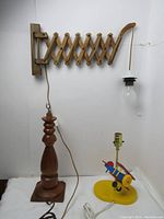 Photo showing all three lamps together against a white backdrop: scissor wall lamp mounted horizontally with a hanging bulb, Danish teak table lamp base, and colorful airplane child table lamp base.