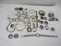 Wide view of entire lot showing various watch parts including cases, backs, straps, and a small wind-up watch.