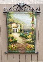 Full view of the vintage textured oil painting on canvas hung on the scrolled metal hanger showing the landscape and floral metal details.