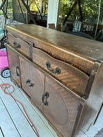 Side view of antique solid hardwood buffet showing wood grain, black metal handles, drawers, and doors.