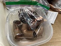 Plastic container with bag labeled '1 inch elbow' containing several small copper elbow fittings.