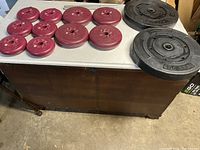 Overall view of all 12 weight plates on table, six smaller red, four medium-sized red, and two large black weight plates.