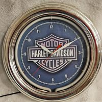 Full view of round Harley Davidson wall clock with blue face, white hour markers, and chrome-colored neon-lit frame.
