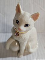 Front view of the white ceramic cat figurine showing detailed facial features and gold collar with pink birthstone pendant.