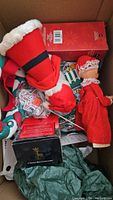 Box filled with assorted Christmas decorations including stocking, dolls, and ornaments