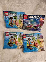 Four new sealed LEGO polybag sets displayed on a fabric surface, showing LEGO Friends and LEGO Dreamzzz packaging.