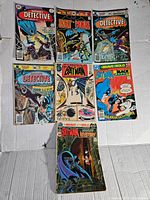 Seven vintage Batman comic books displayed on a white surface showing cover art and condition variations.