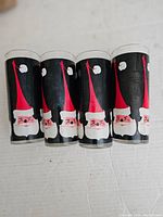 Four vintage mid-century glasses with Santa Claus design, black background, red hat and white beard, no chips or cracks visible.